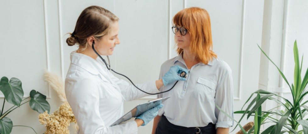 Médica a fazer um check up médico completo a uma mulher sorridente.